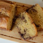 A loaf of fresh milled cinnamon swirl bread with two slices on a wooden cutting board.