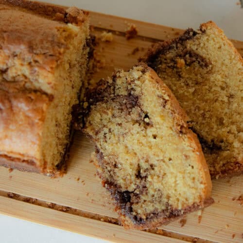 A loaf of fresh milled cinnamon swirl bread with two slices on a wooden cutting board.