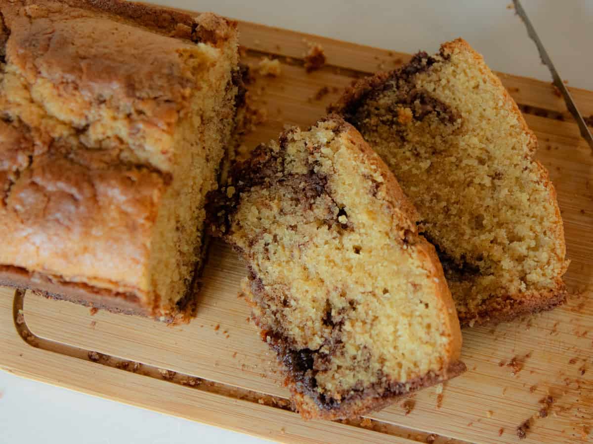 A loaf of fresh milled cinnamon swirl bread with two slices on a wooden cutting board.