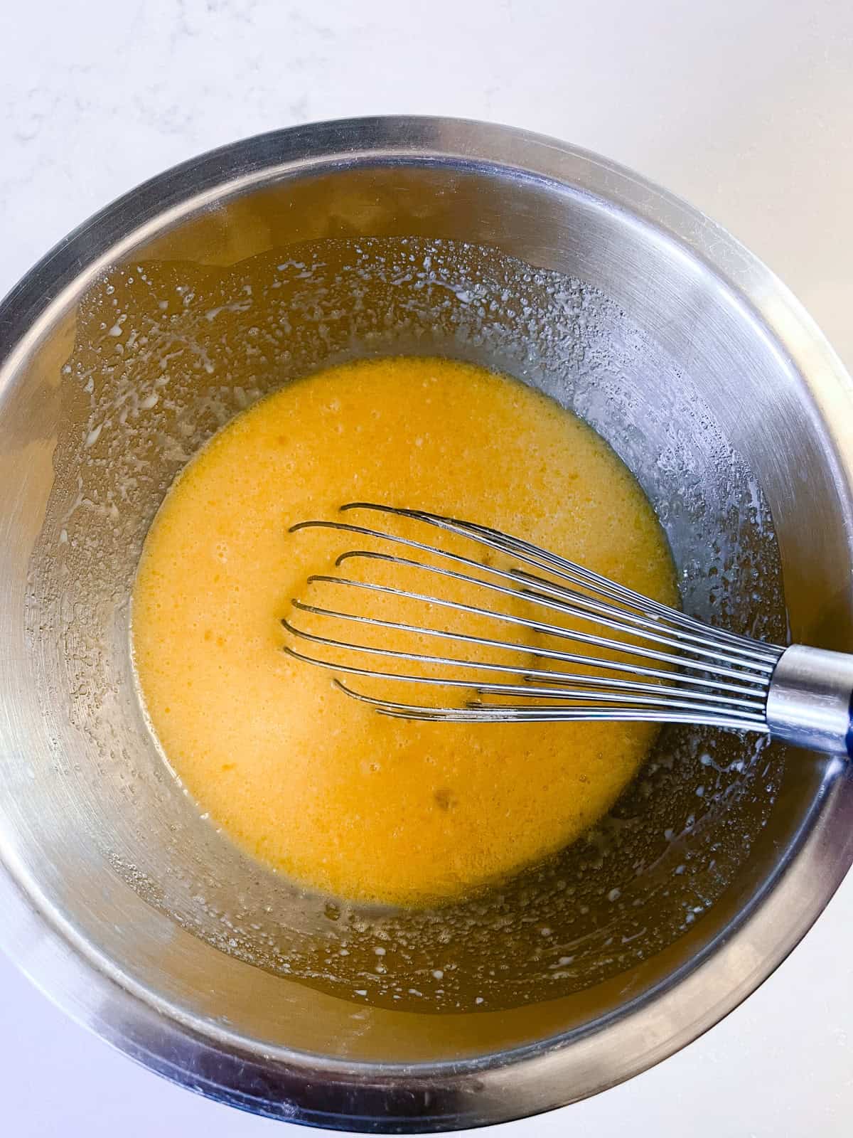 Whisking wet ingredients together in a metal mixing bowl.