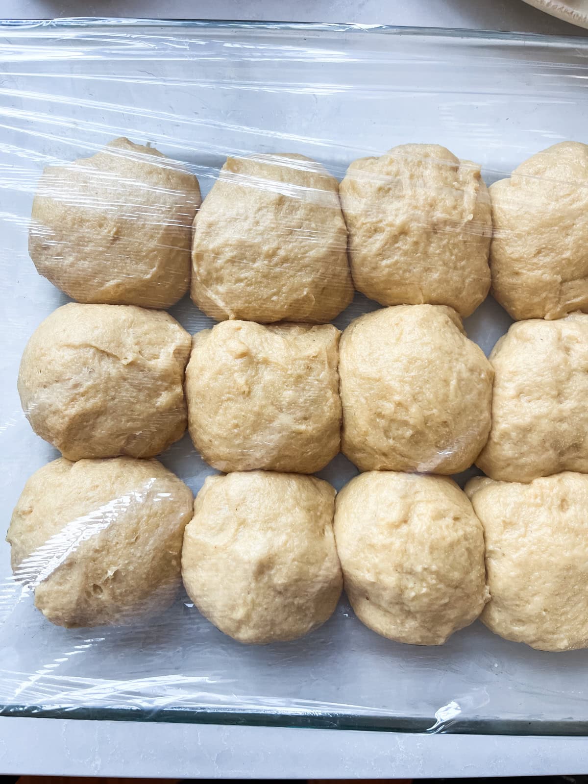 Fresh milled flour Hawaiian rolls fully risen on a baking sheet covered with plastic wrap.