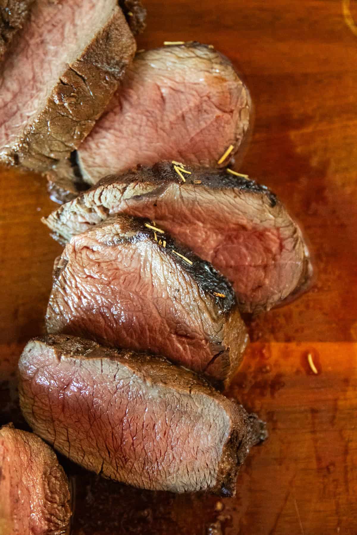 Strips of marinated venison backstrap on a wooden cutting board.