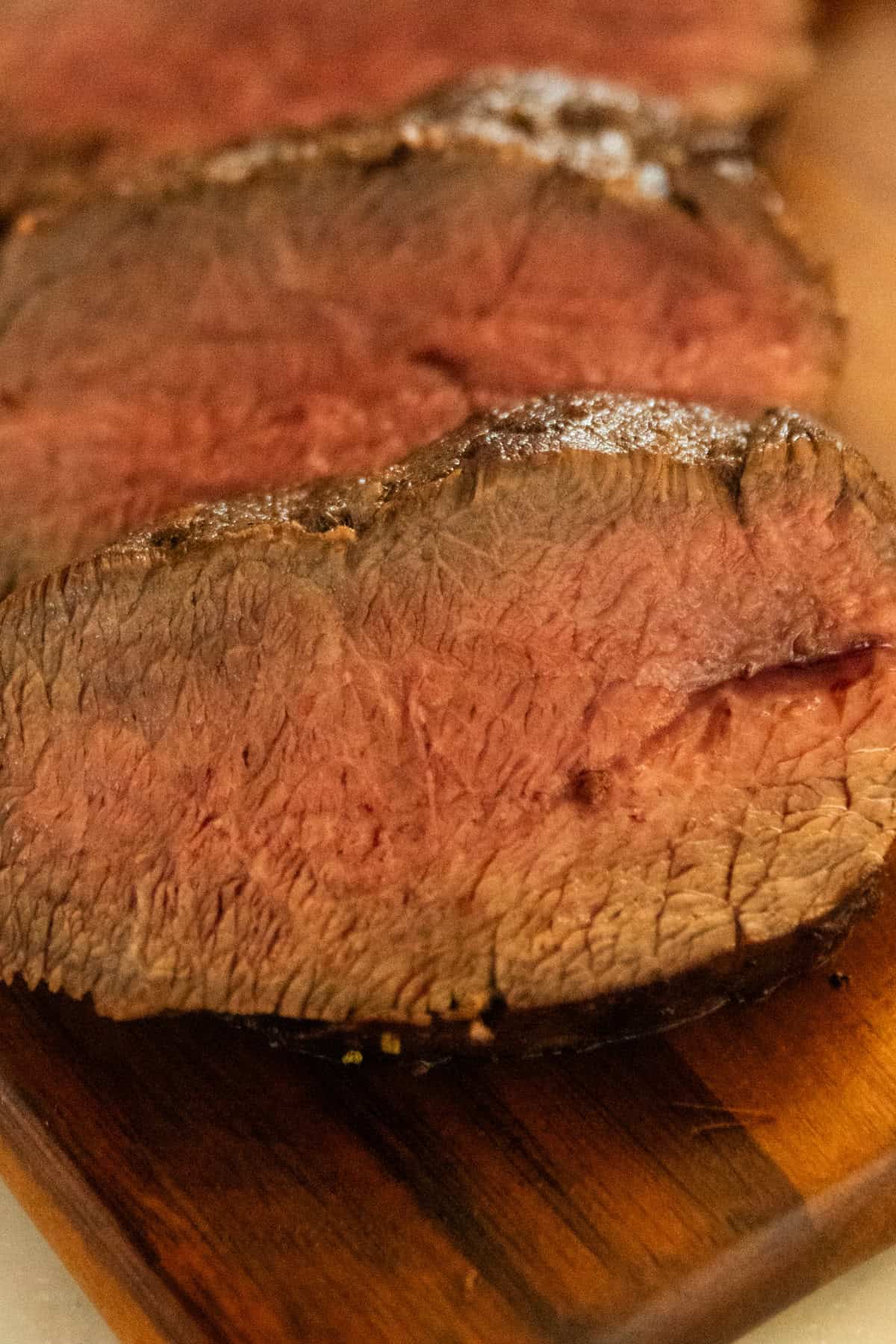A close-up of slices of venison backstrap on a wooden board.