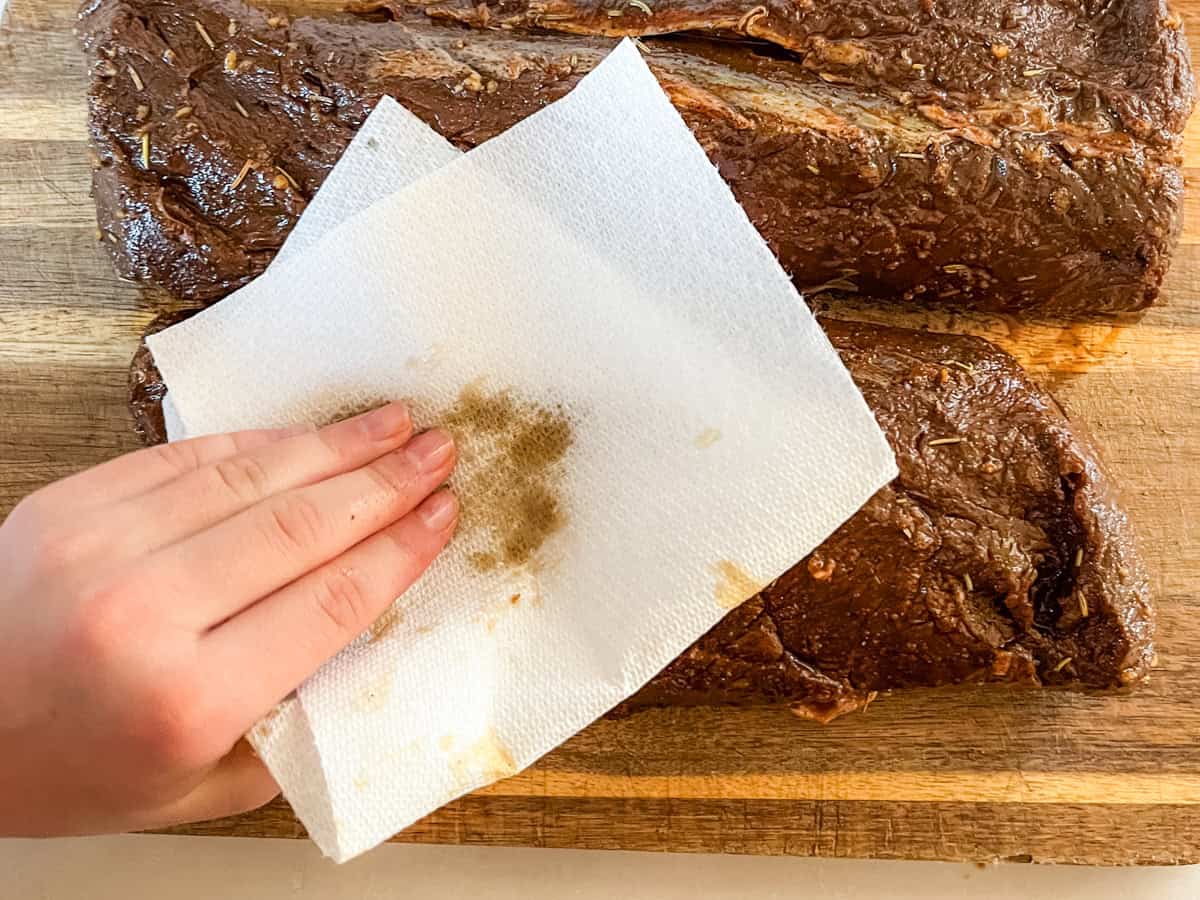 Patting dry the marinated venison backstrap with paper towels.