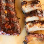 A rack of baby back ribs on a wooden cutting board with sliced ribs next to it.