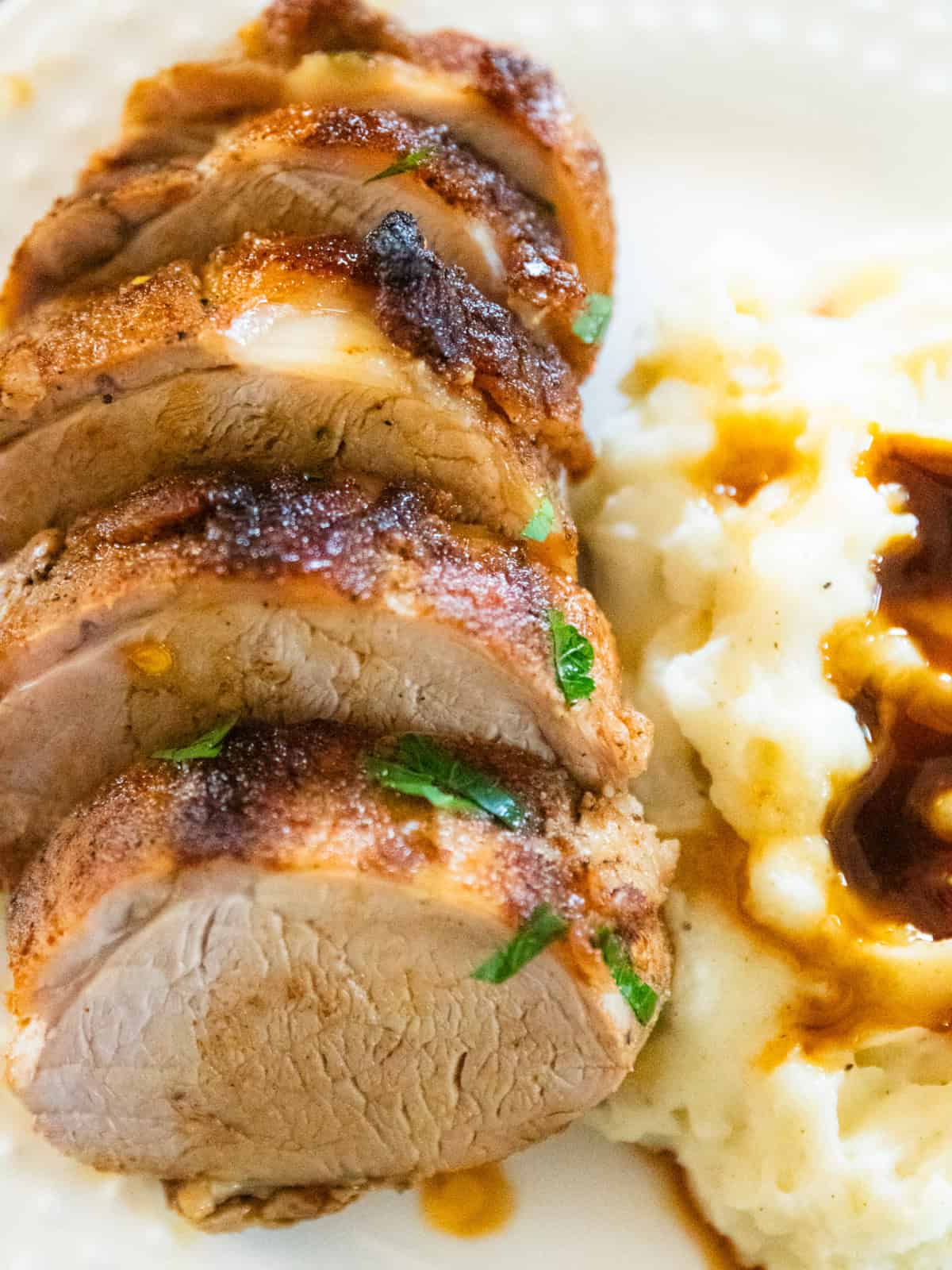 Baked pork catfish tenderloin on a white plate with mashed potatoes and gravy. 