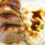 Baked pork catfish tenderloin next to a serving of mashed potatoes and gravy on a white plate.