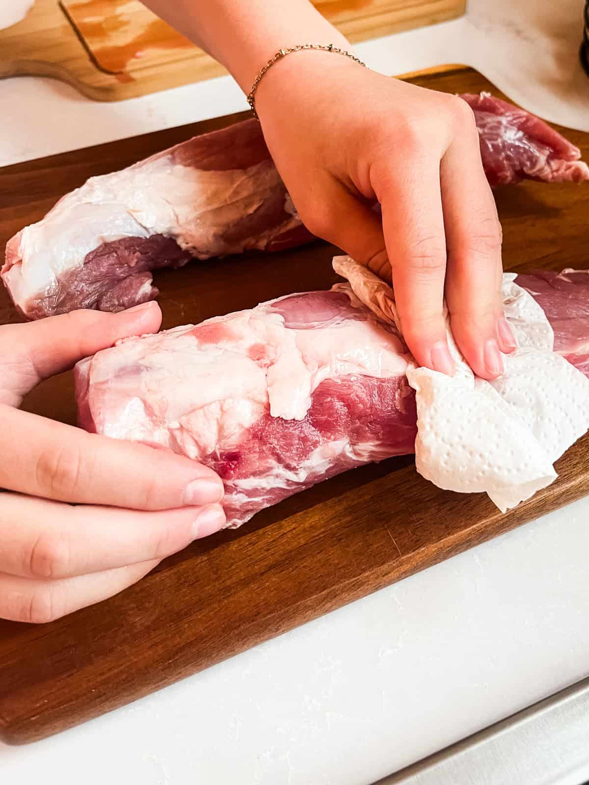 Patting dry a raw pork tenderloin.