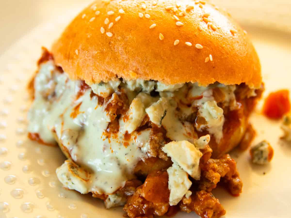 A buffalo chicken sloppy joe on a white plate with ranch and blue cheese.