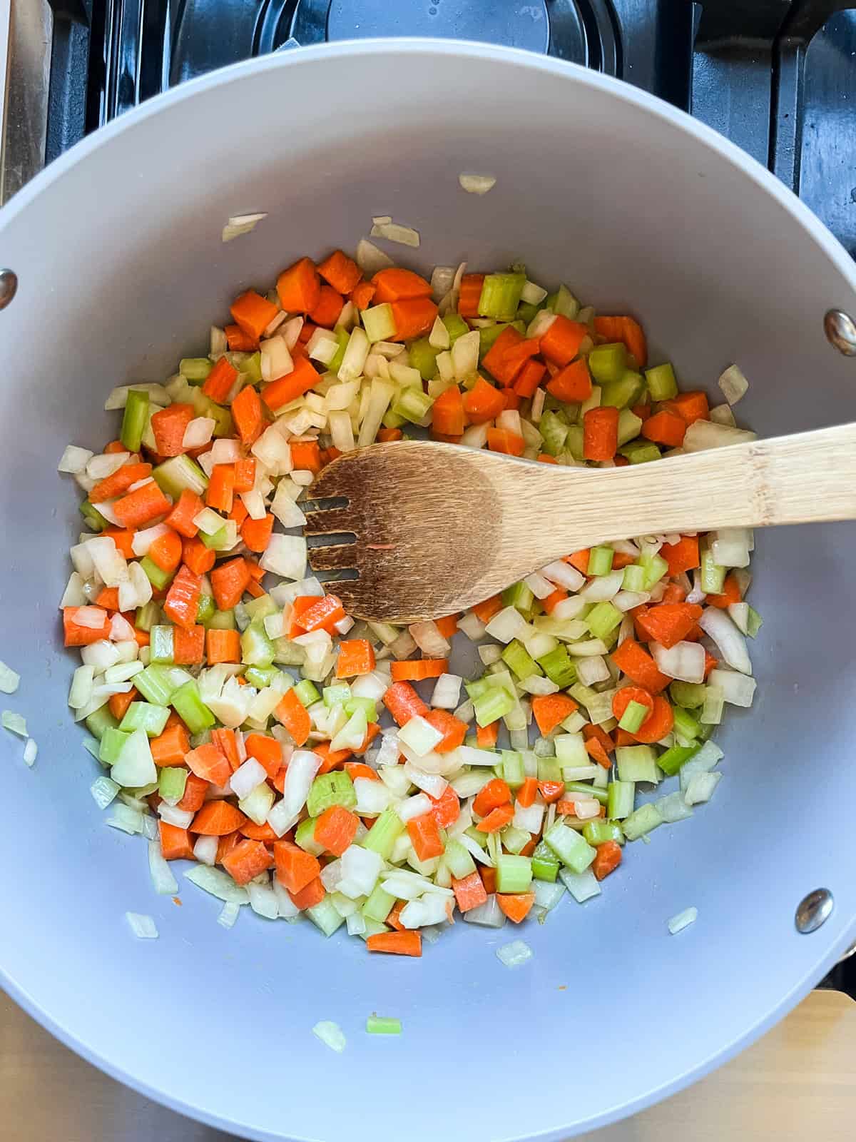 Sauteing carrots, onions, and celery in a pot with a wooden spoon.