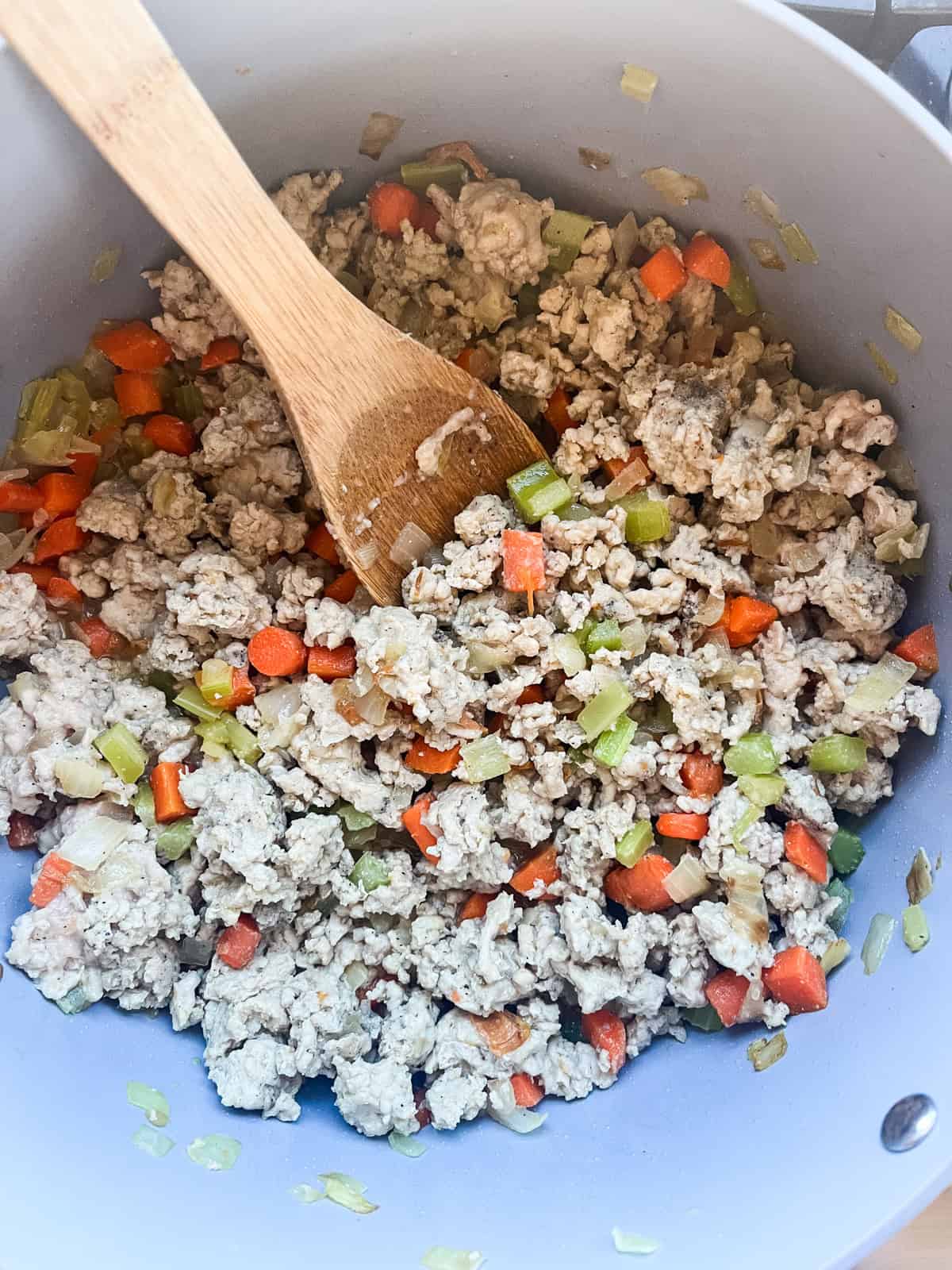 Cooking ground chicken in the pot with carrots, celery, and onions.
