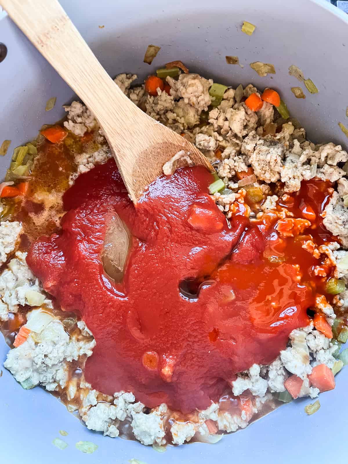 Adding tomato sauce and other liquid ingredients to a pot of sloppy joe meat.