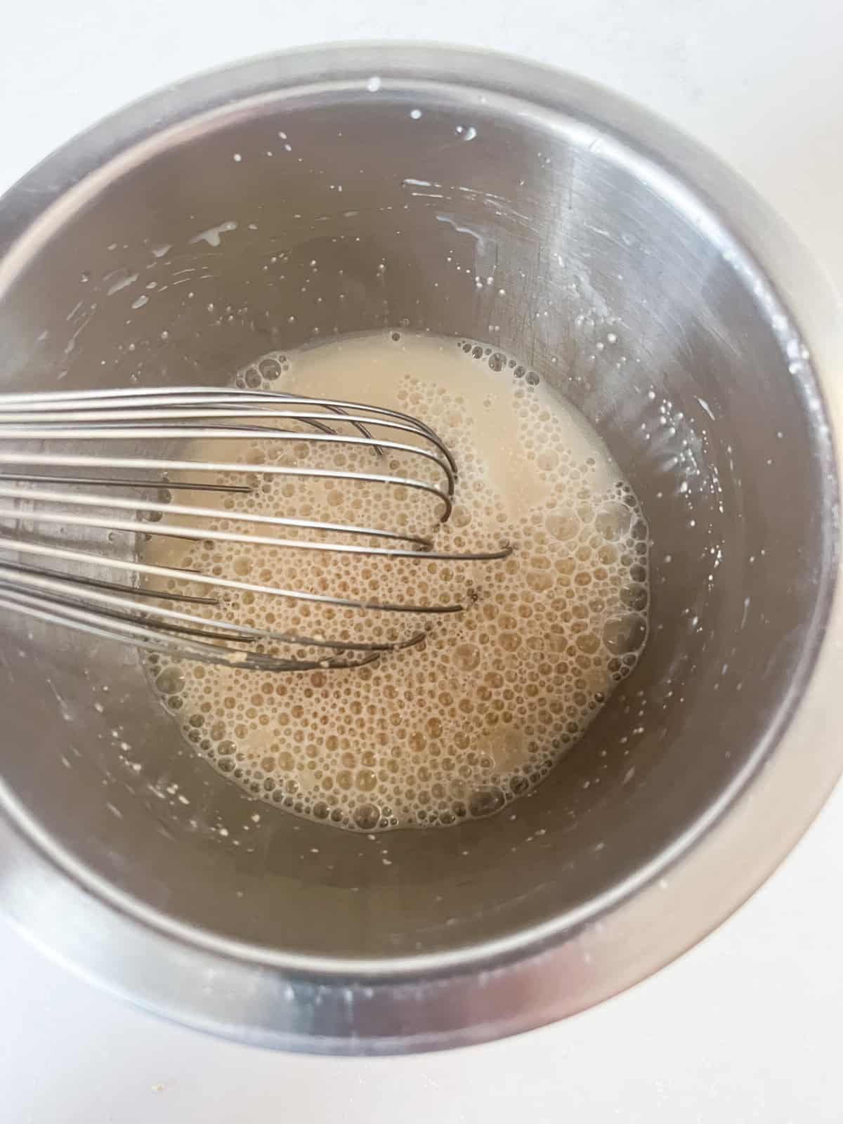 Whisking yeast and water together in a metal bowl.