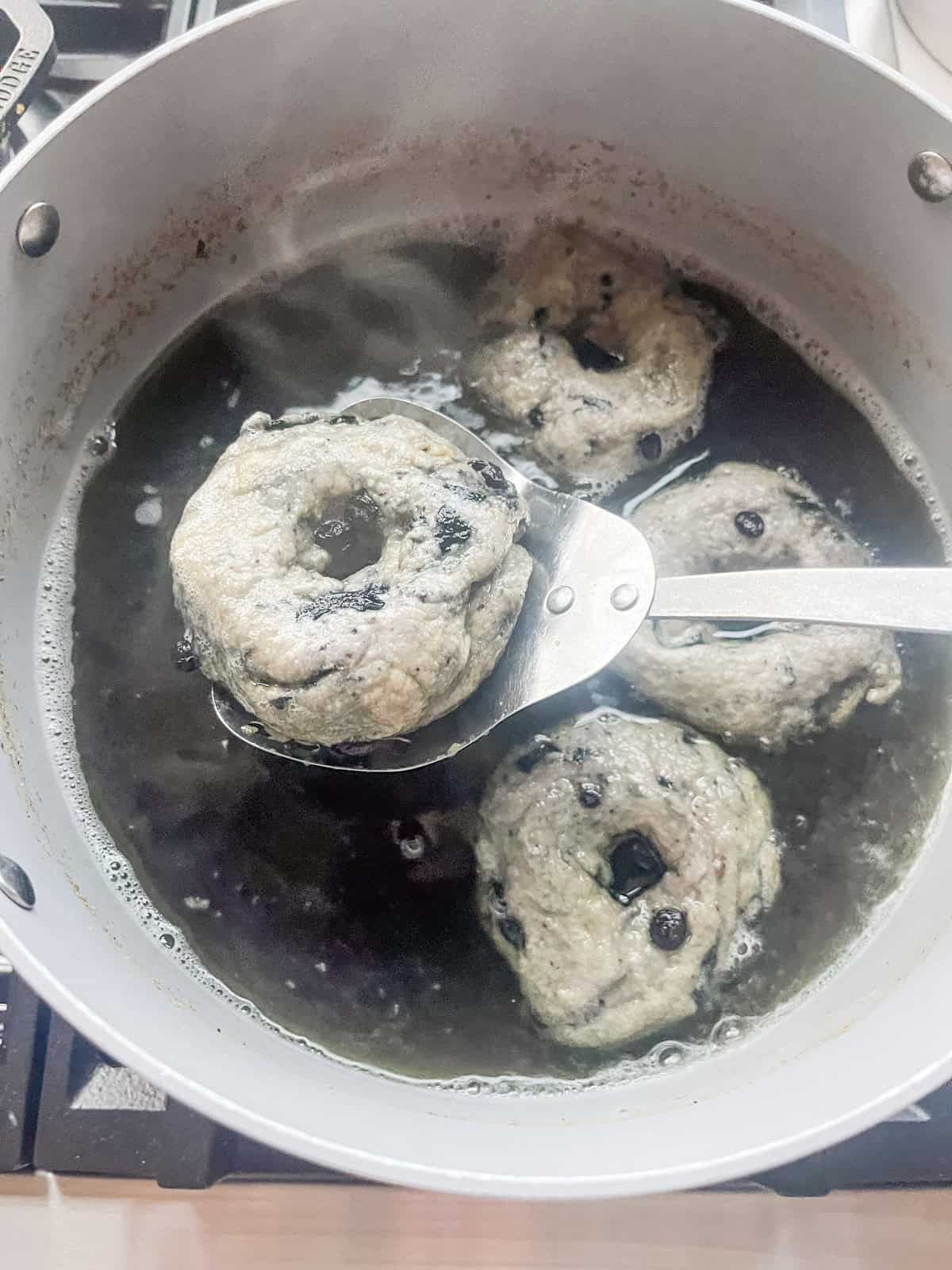 Scooping a blueberry bagel out of a pot of boiling water.