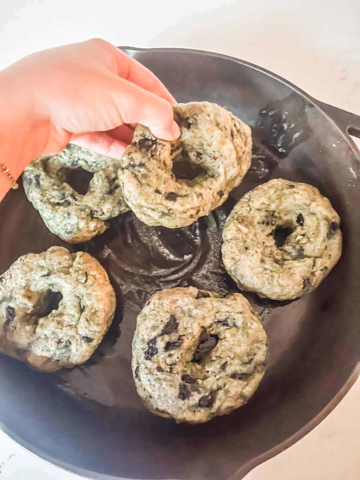 Placing boiled blueberry bagels in a cast iron skillet.