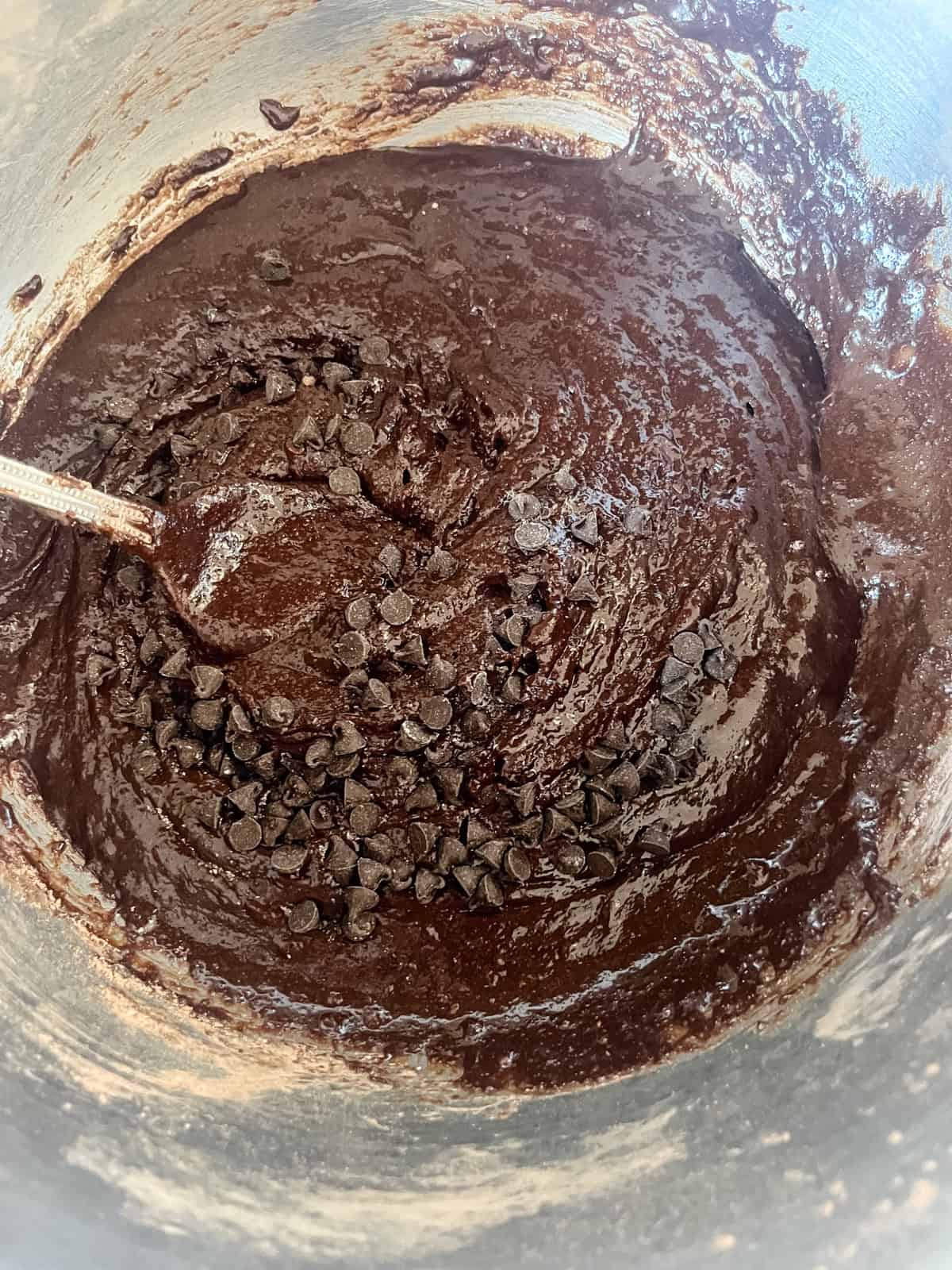 Mixing chocolate chips into brownie batter with a spoon.