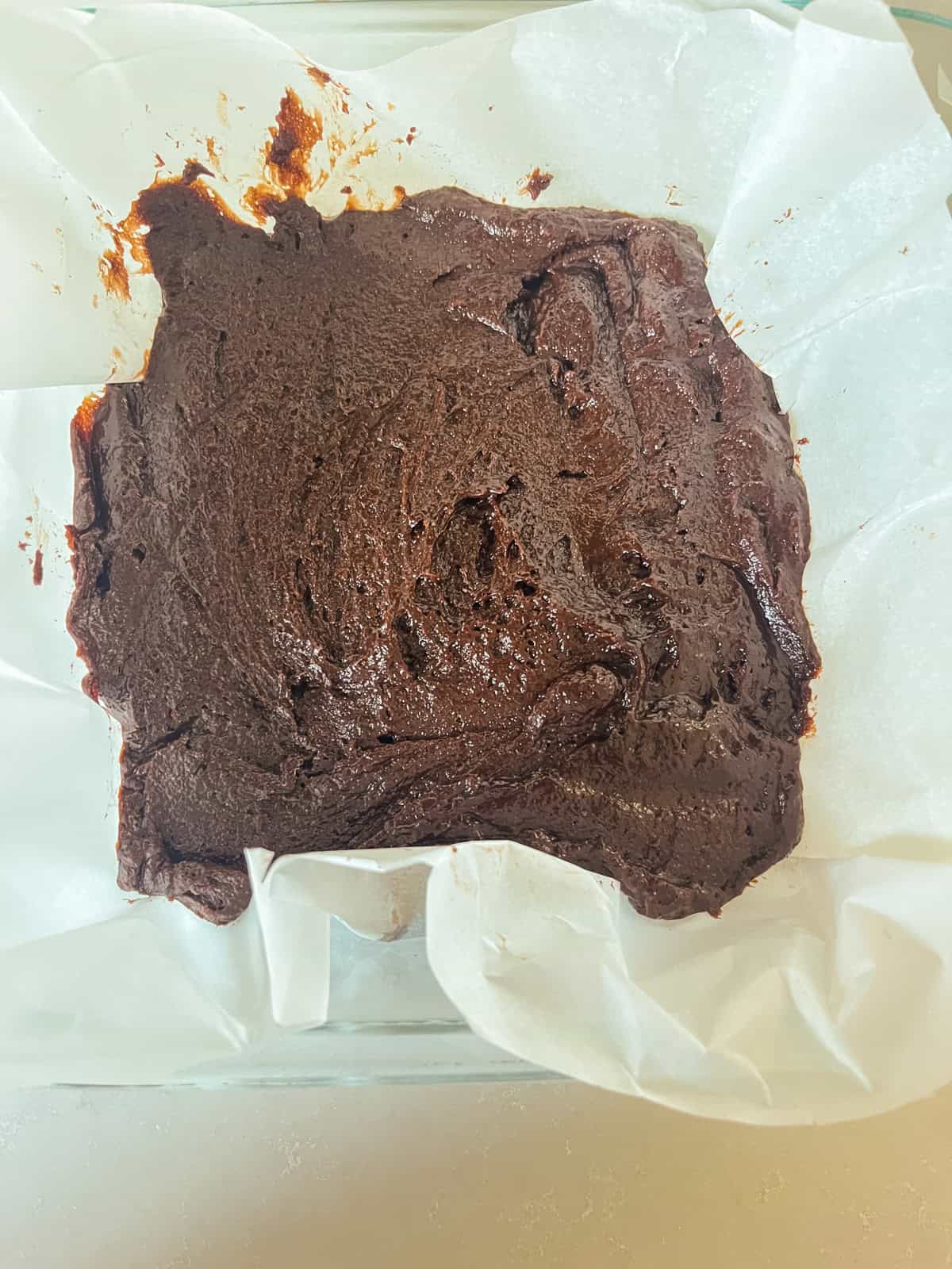 Brownie batter spread into a lined baking dish.