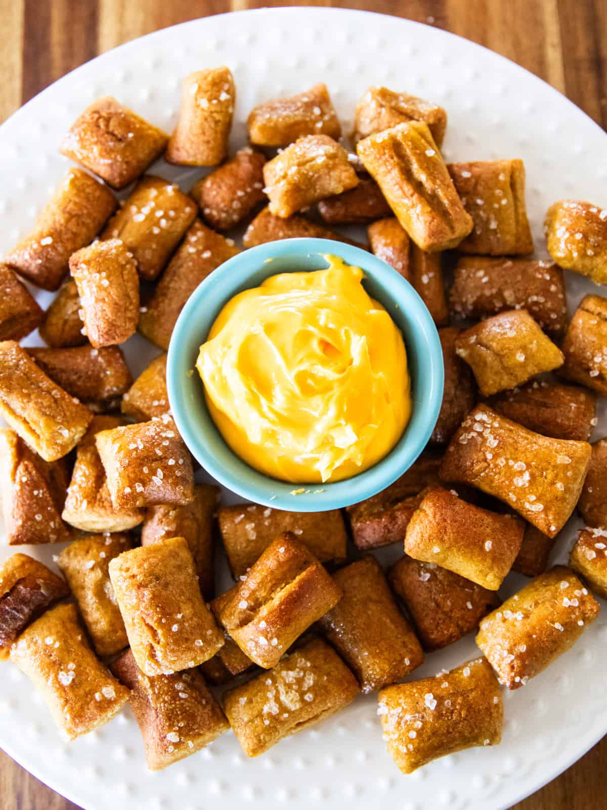 Fresh milled pretzel bites on a white platter with cheese in a small bowl in the center.