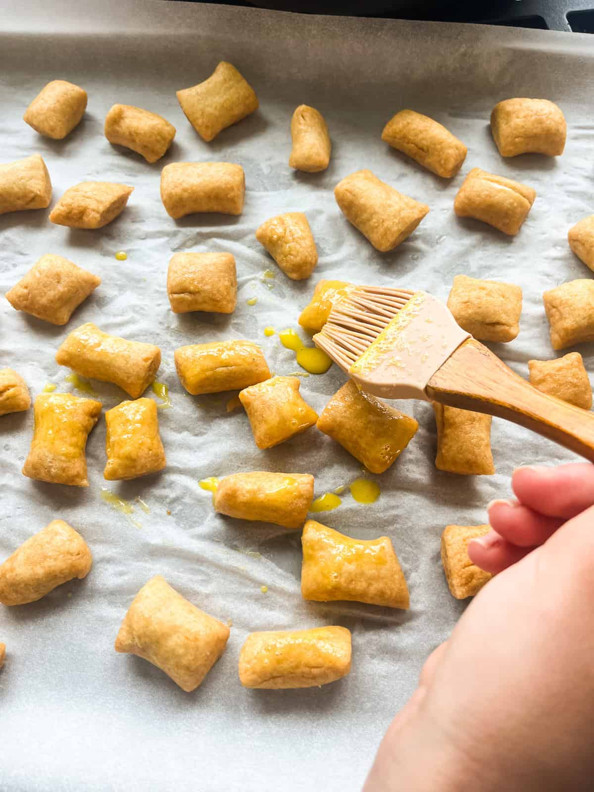Brushing boiled pretzel bites with egg wash on a sheet pan.