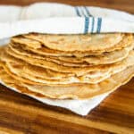 A stack of freshly milled tortillas wrapped in a striped towel on a wooden table.