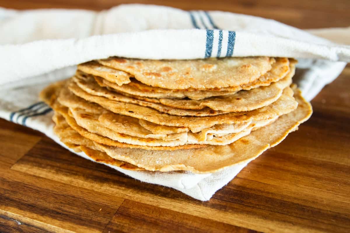 A stack of freshly milled tortillas wrapped in a striped towel on a wooden table.