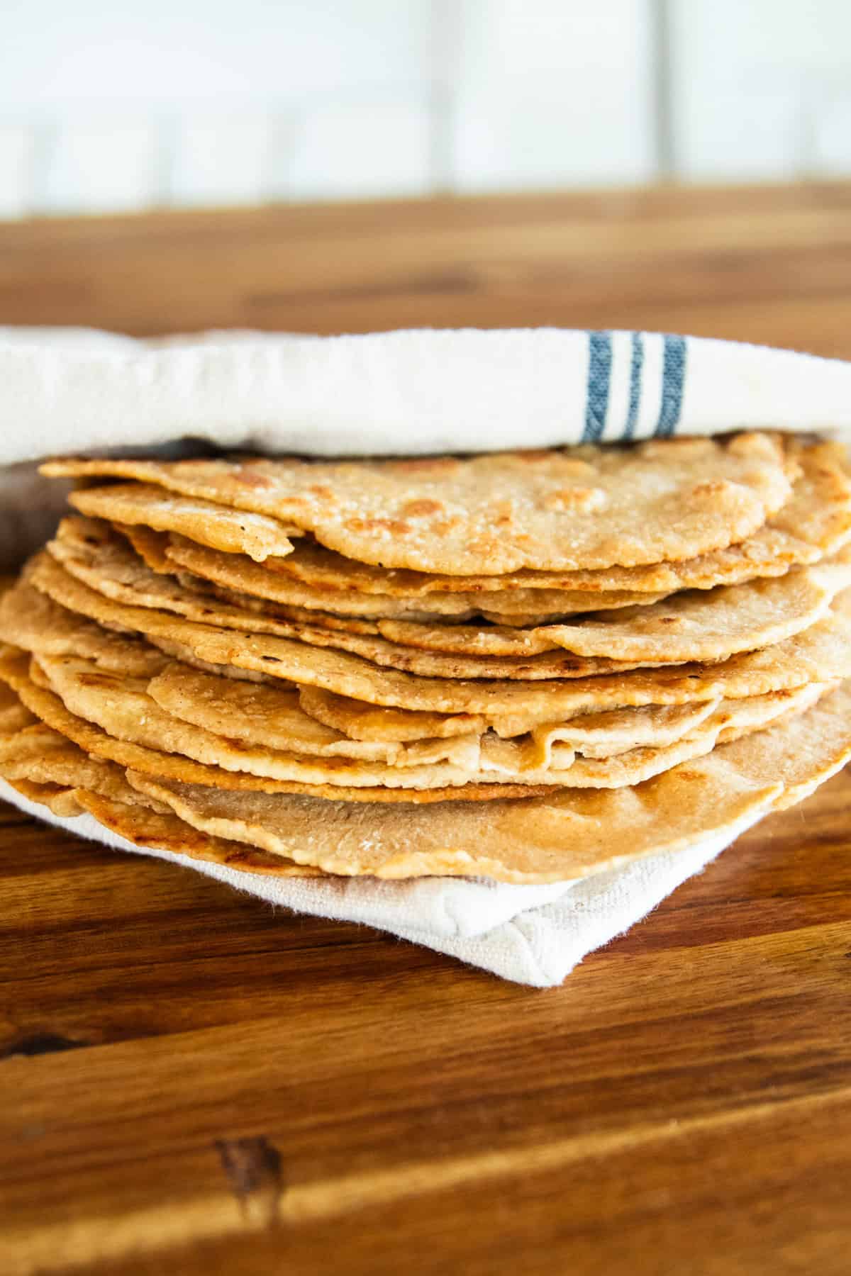 Freshly milled tortillas stored in a towel on a butcher block table.