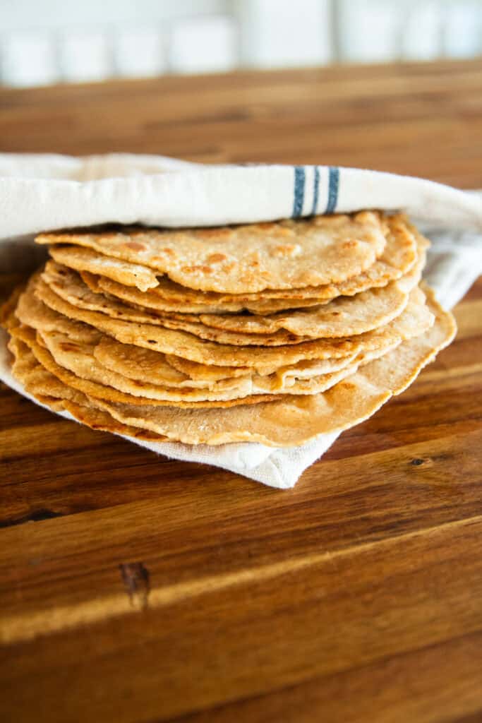 A stack of freshly milled tortillas folded into a towel on a wooden table.