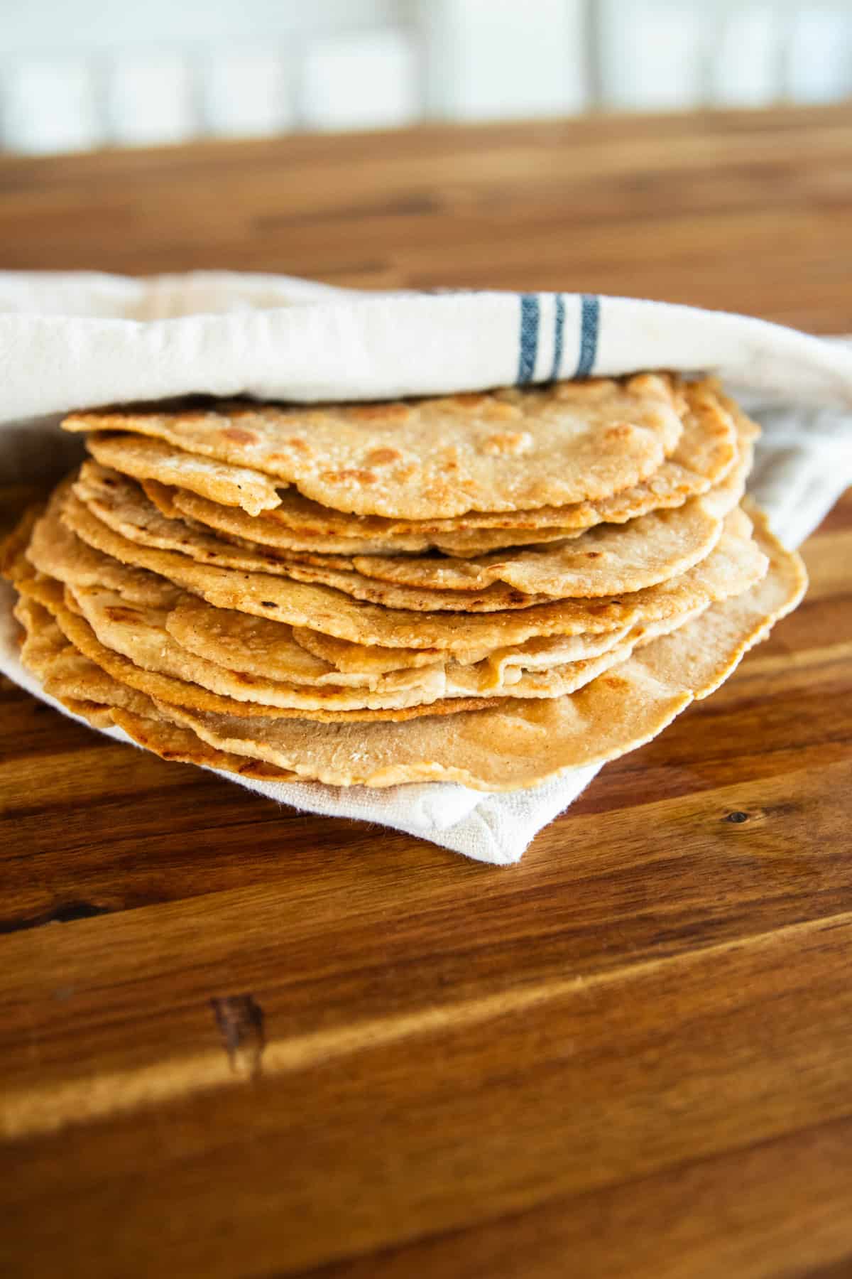 A stack of freshly milled tortillas folded into a towel on a wooden table. 
