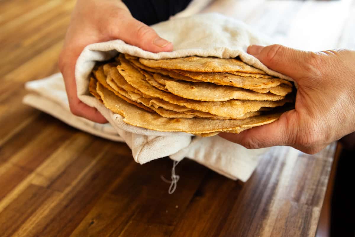 Holding a stack of freshly milled tortillas wrapped in a white towel.