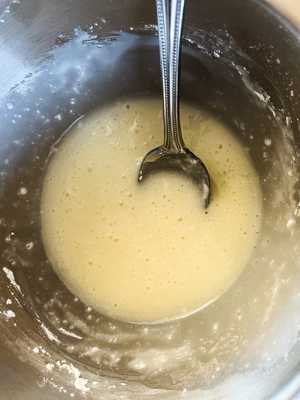 Stirring yeast and milk in a metal mixing bowl.
