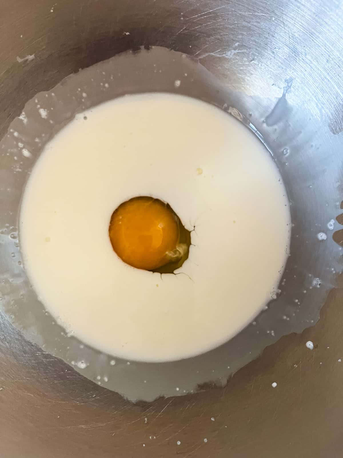 An egg and milk in a metal mixing bowl.