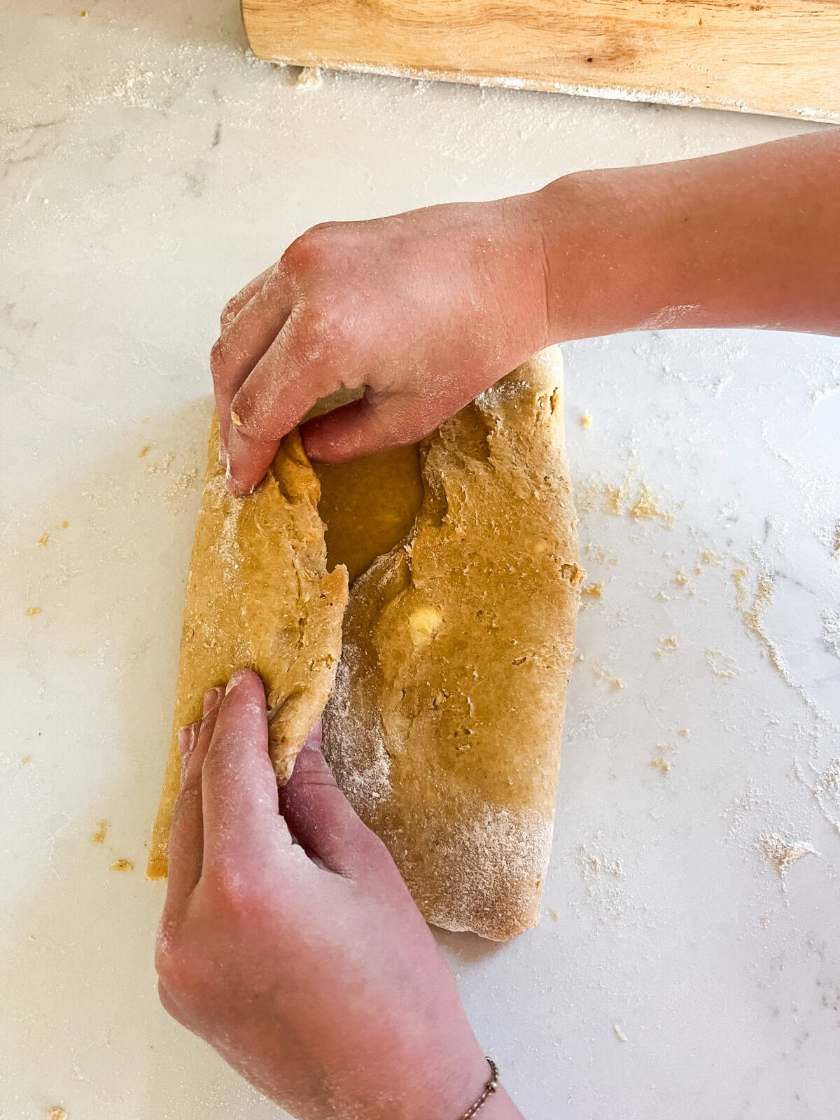 Flattening and folding fresh milled donut dough.