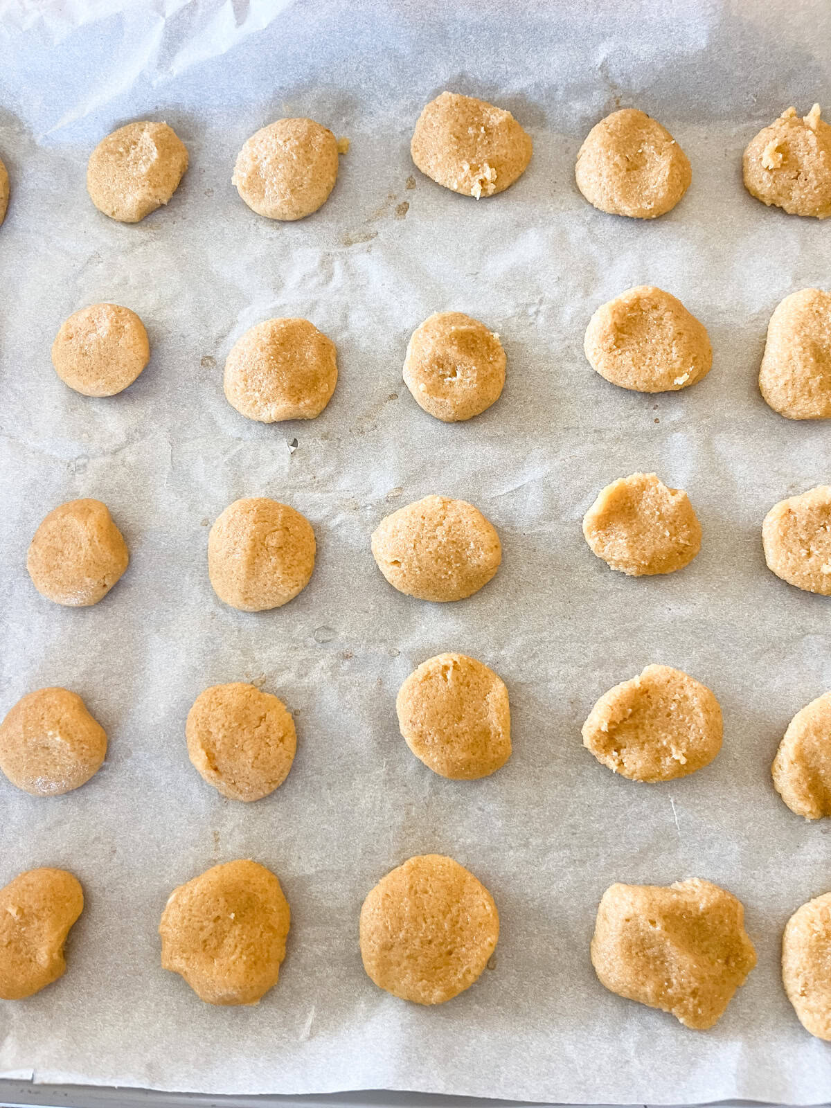 Unbaked vanilla wafers lined up on a parchment paper-lined baking sheet.