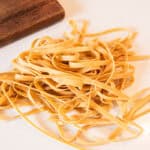 Strands of homemade whole wheat noodles on a white countertop.