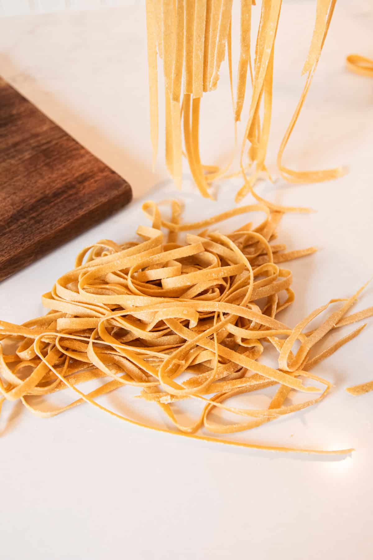 Homemade whole wheat noodles freshly made on a quartz countertop with more noodles hanging on a noodle rack behind them.