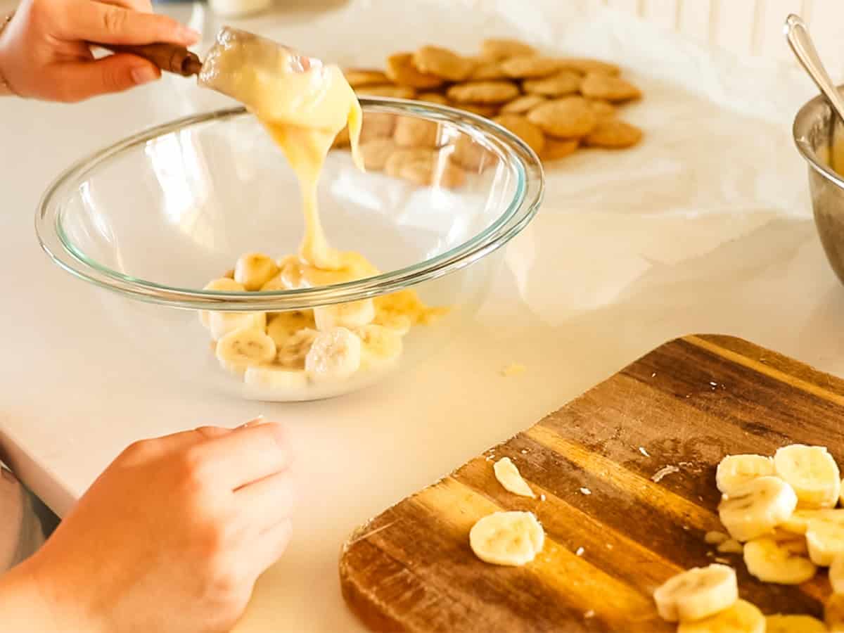 Scooping vanilla pudding into the bowl of banana slices.