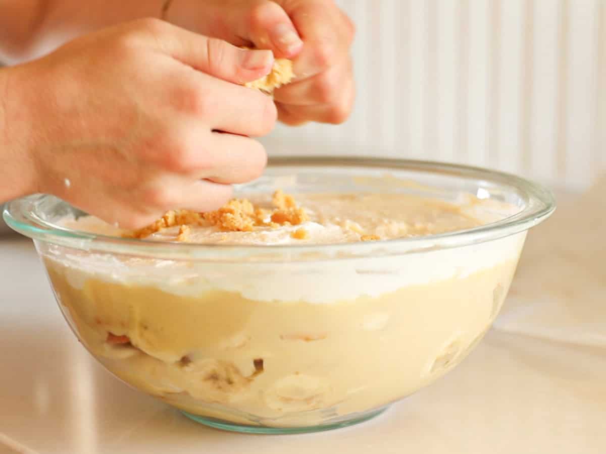 Sprinkling crushed vanilla wafers on top of the banana pudding.