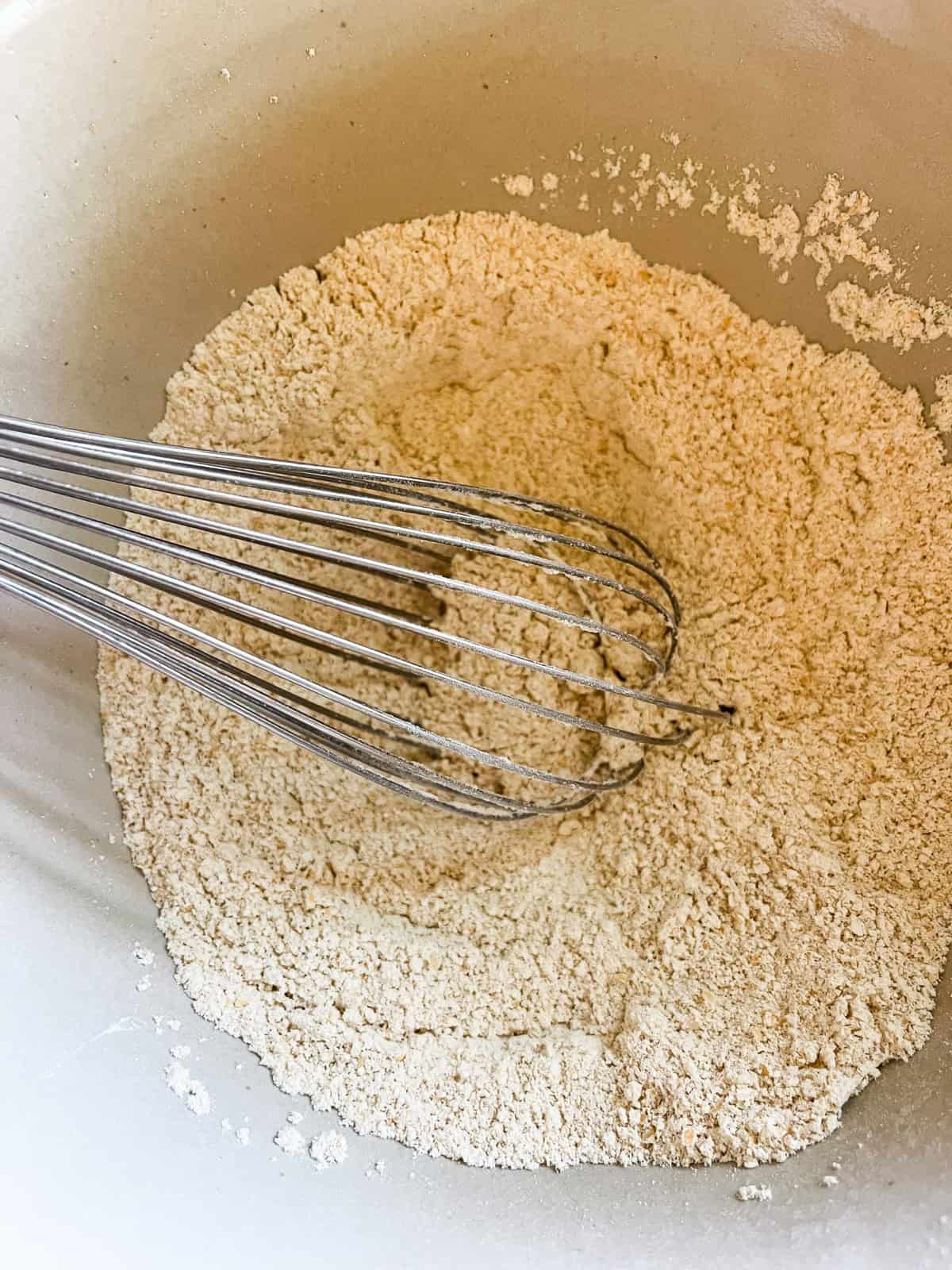 Stirring dry ingredients with a whisk in a mixing bowl.