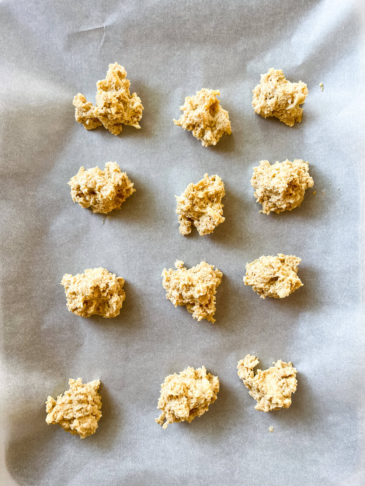 Cheddar biscuit dough scooped onto a parchment paper-lined baking sheet.