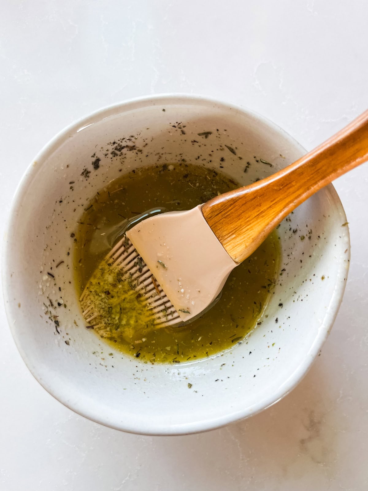 A bowl of melted garlic butter with a silicone pastry brush.