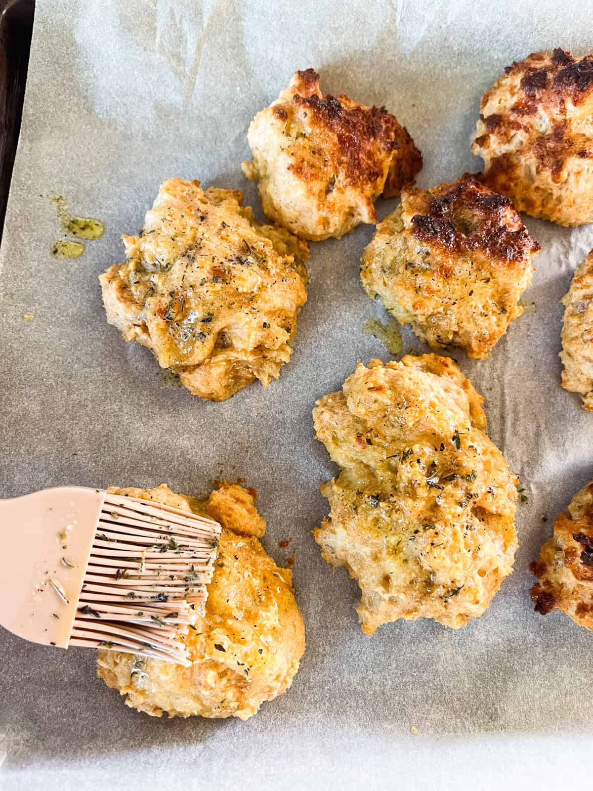 Brushing garlic butter onto baked cheddar biscuits with a pastry brush.