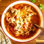 A bowl of Dutch oven pizza soup with cheese on top with a spoon and napkin.