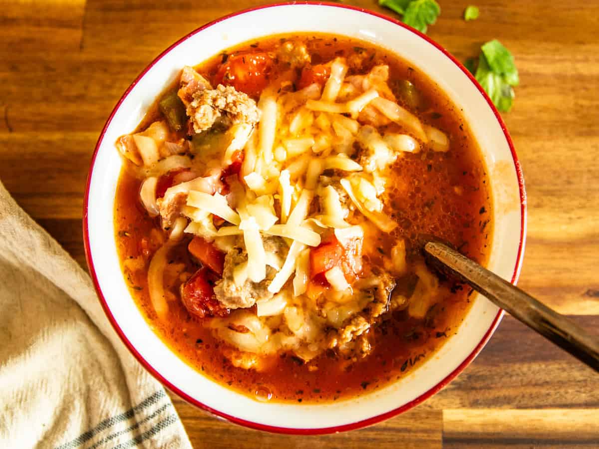 A bowl of Dutch oven pizza soup with cheese on top with a spoon and napkin.