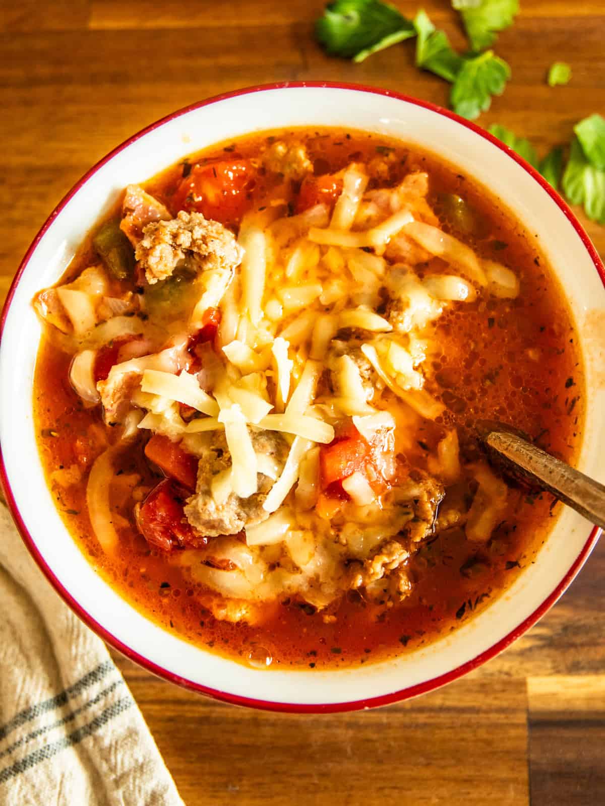 A bowl of Dutch oven pizza soup with a spoon sticking out of it and a napkin to the side.