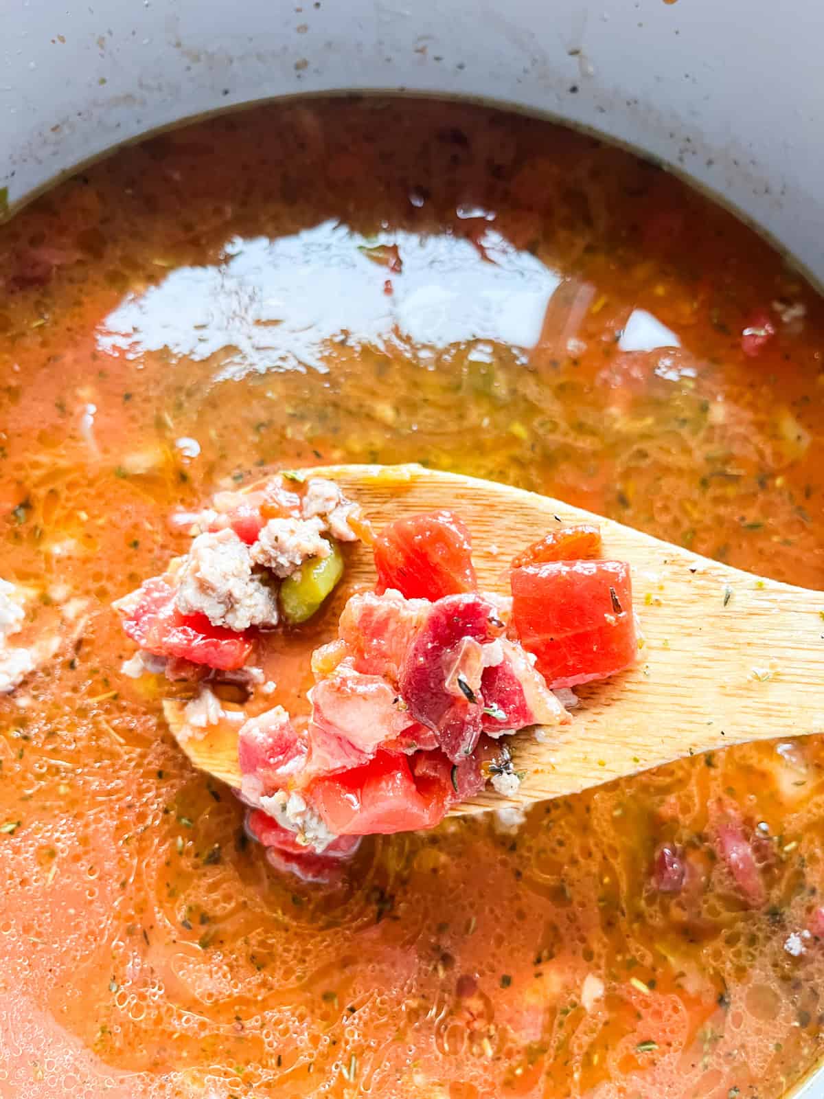 Scooping a spoonful of pizza soup out of a Dutch oven with a wooden spoon.
