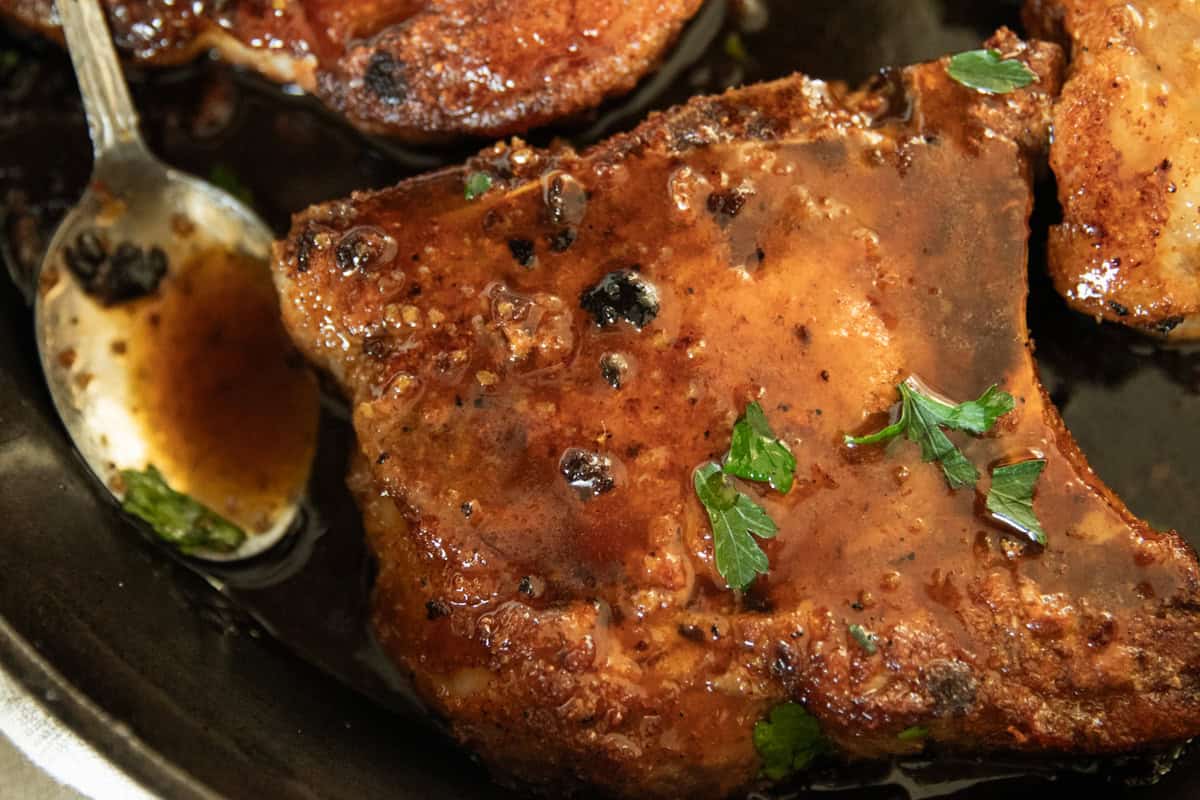 A pan-fried pork chop in a cast iron skillet with a spoon and sauce.