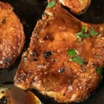 Two pan-fried pork chips in a cast iron skillet.
