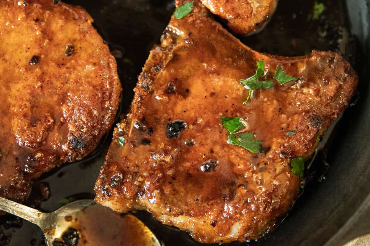 Two pan-fried pork chips in a cast iron skillet.