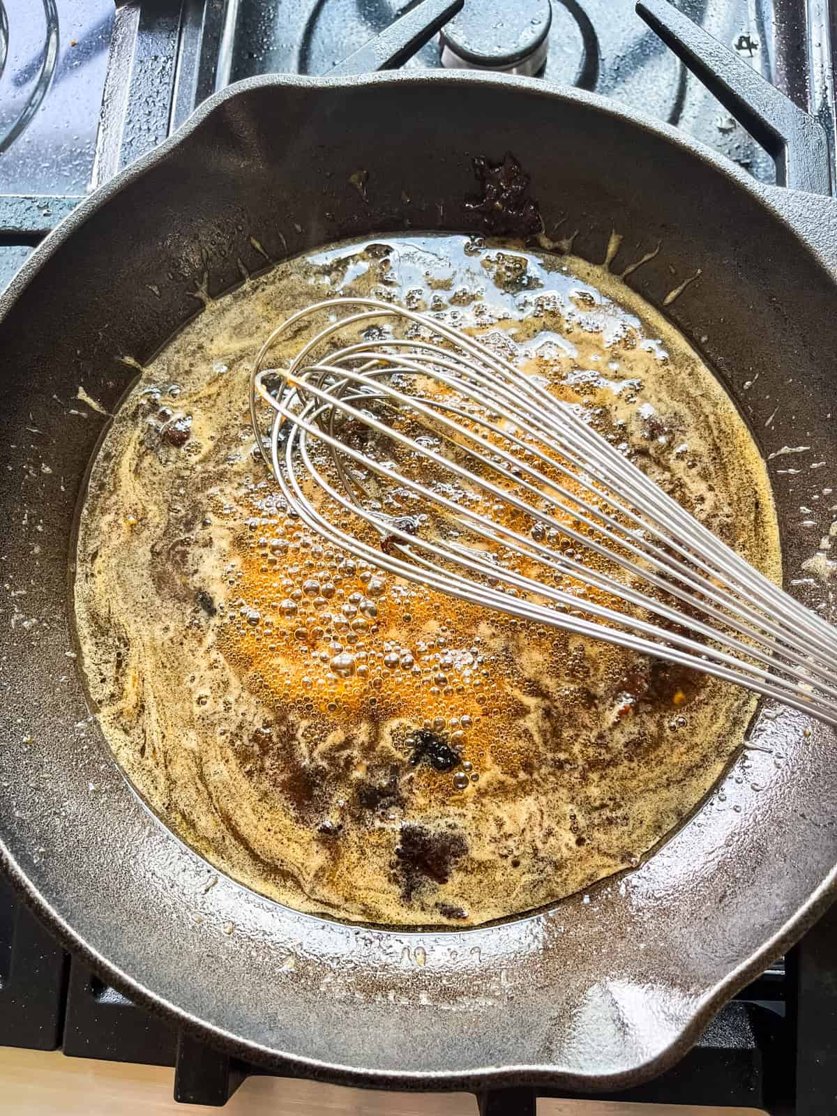 Stirring sauce in a cast iron skillet with a whisk.