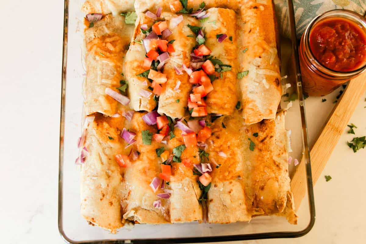 A pan of venison enchiladas with a jar of salsa on the side.